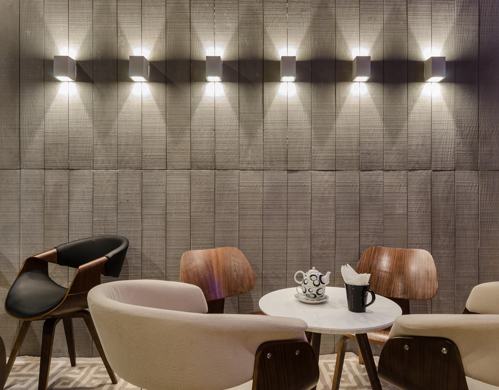Ambiente com duas mesas de café, ao fundo parede com revestimento concrewood e alguns pontos de luz.