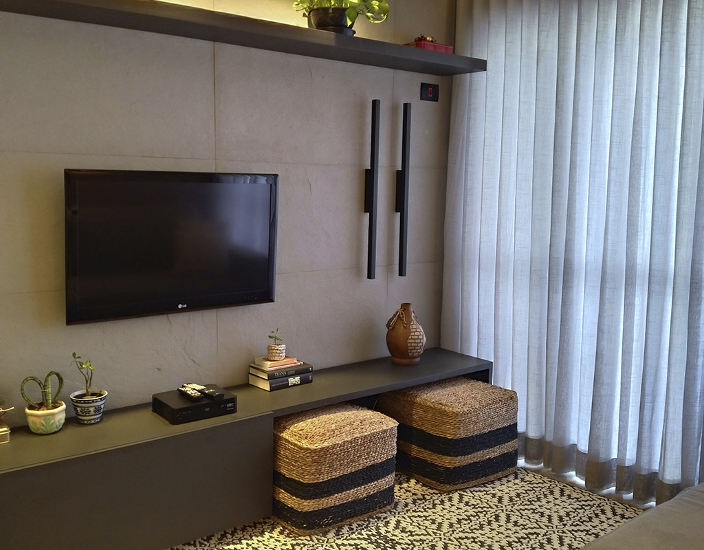 Sala de estar com painel de tv com o revestimento Estônia, com um rack cinza baixo, com alguns objetos de decoração e dois pufs de sisal.