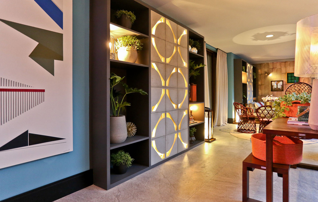 O ambiente da foto mostra uma parede azul e um quadro decorativo, um armário com plantas e no centro uma inserção no móvel com o revestimento angolo iluminado